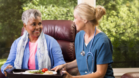 Home healthcare nurse with senior adult patient. Meal.